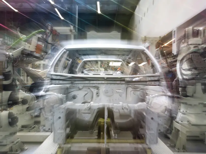 A car body moving along an assembly line between robotic arms, blurred with motion