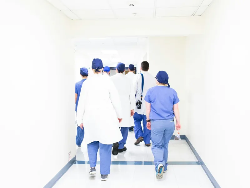A clinical team in scrubs and white coats walking down a bright hospital corridor