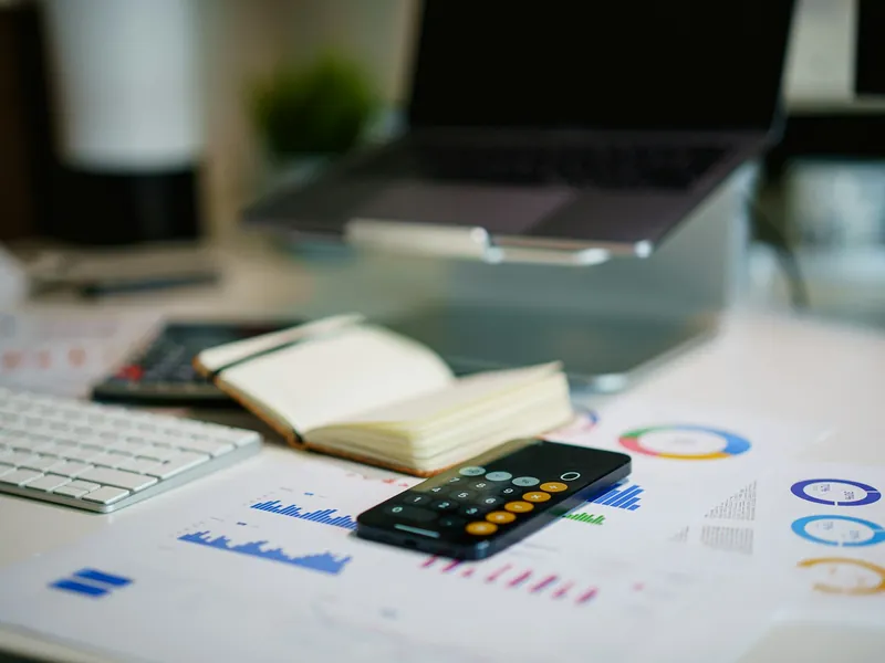 Printed financial charts, a notebook and a calculator on an office desk