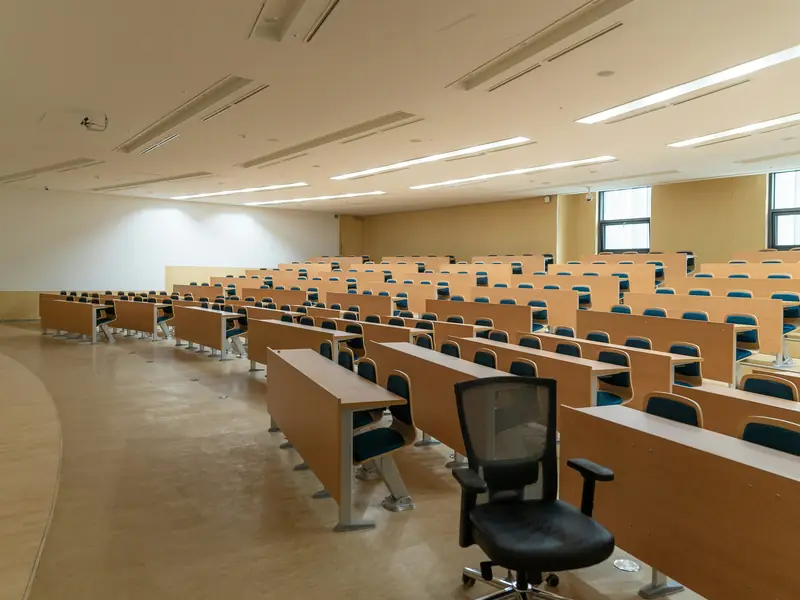 Rows of empty wooden desks and chairs in a bright university lecture hall