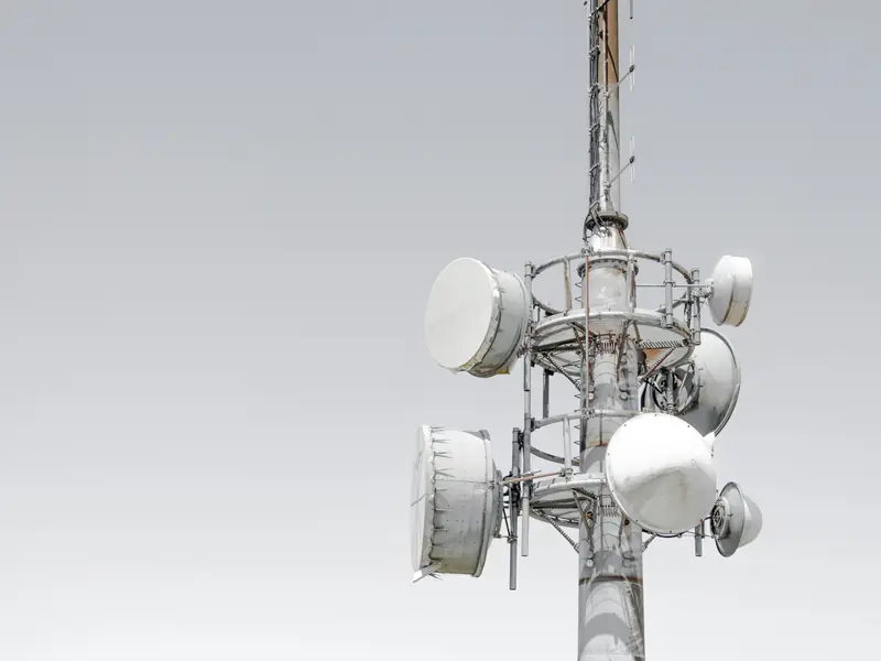 A telecommunications tower with round microwave antennas against a grey sky